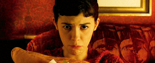 Imagem em movimento de uma cena do filme "o fabuloso destino de Amélie Poulain". A protagonista, interpretada por Audrey Tautou, encara a câmera e mastiga com dificuldade um pedaço de pão.
