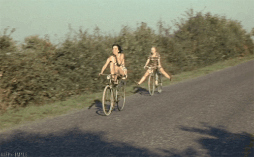 Garotas andam de bicicleta numa descida sem colocar os pés nos pedais.