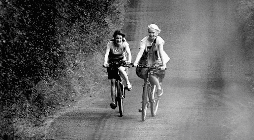 Duas garotas alegres andam de bicicleta numa estrada de terra.